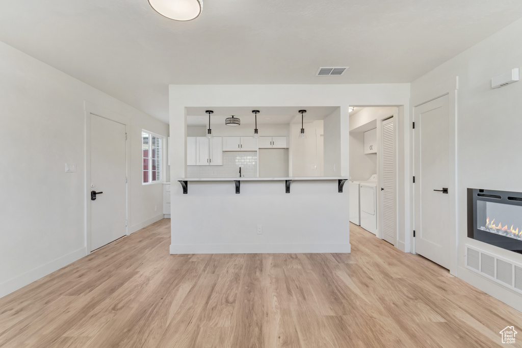 Kitchen featuring tasteful backsplash, light hardwood / wood-style floors, white cabinetry, and a kitchen bar