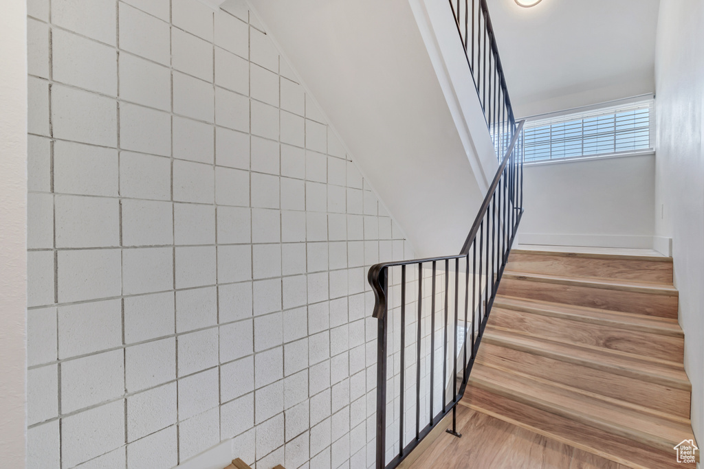Stairway with light hardwood / wood-style floors and tile walls