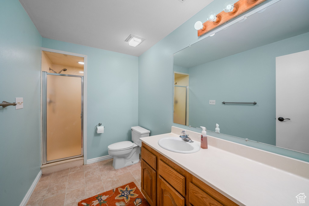 Bathroom with vanity with extensive cabinet space, a shower with shower door, tile floors, and toilet
