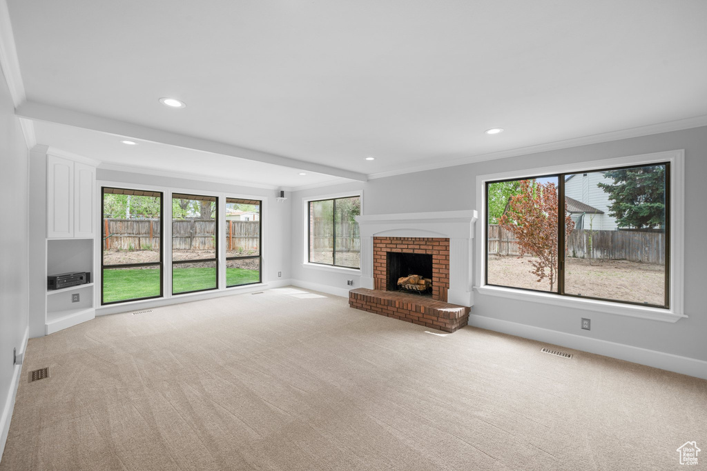 Unfurnished living room with light colored carpet, ornamental molding, and a brick fireplace