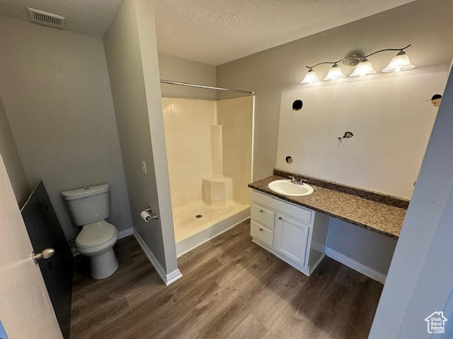 Bathroom with walk in shower, vanity, hardwood / wood-style flooring, toilet, and a textured ceiling