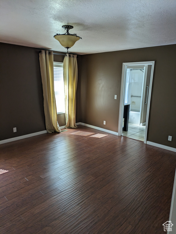 Empty room with dark hardwood / wood-style floors and a textured ceiling
