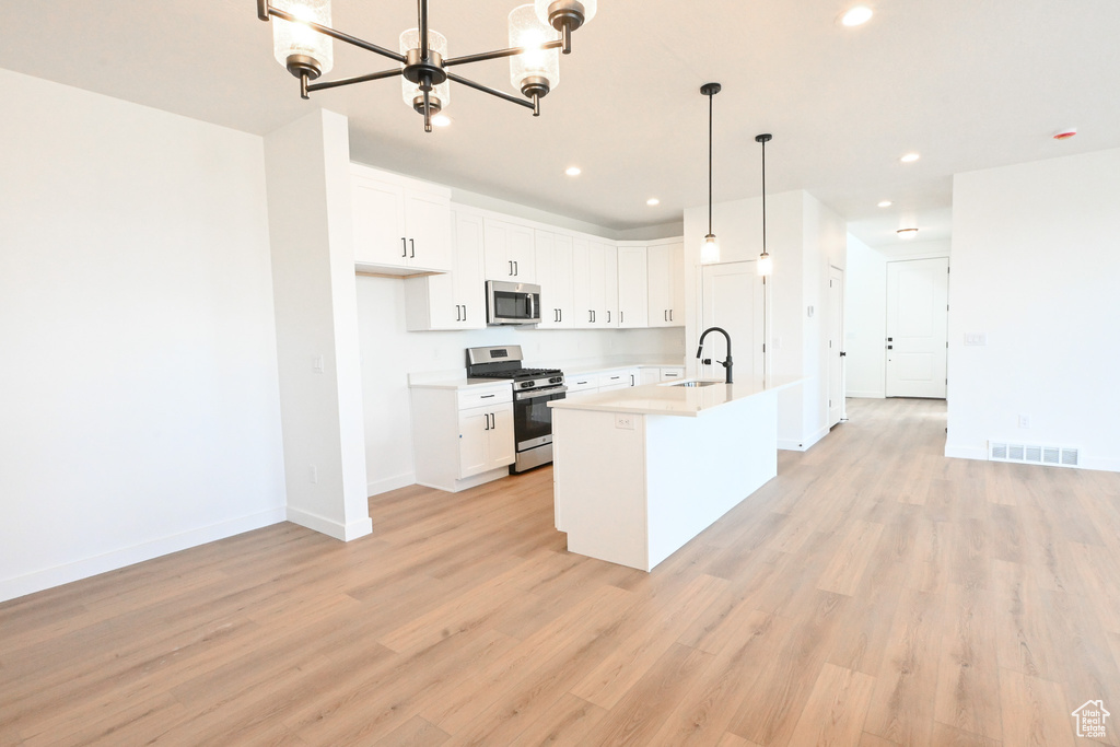 Kitchen featuring appliances with stainless steel finishes, light hardwood / wood-style floors, white cabinetry, decorative light fixtures, and a center island with sink