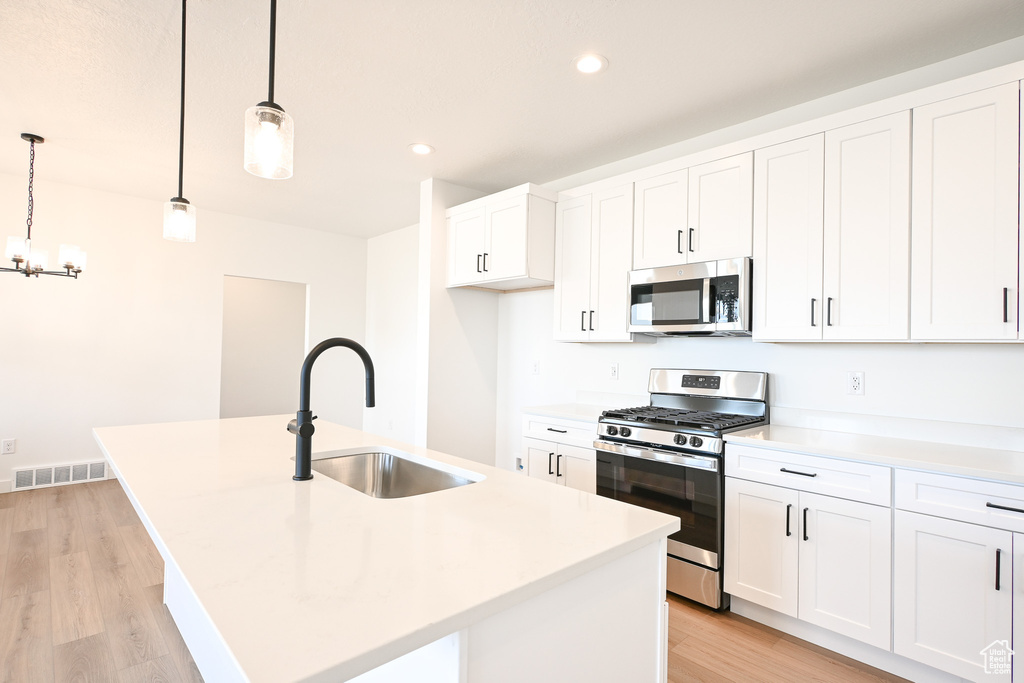 Kitchen featuring white cabinets, sink, light hardwood / wood-style floors, stainless steel appliances, and a center island with sink
