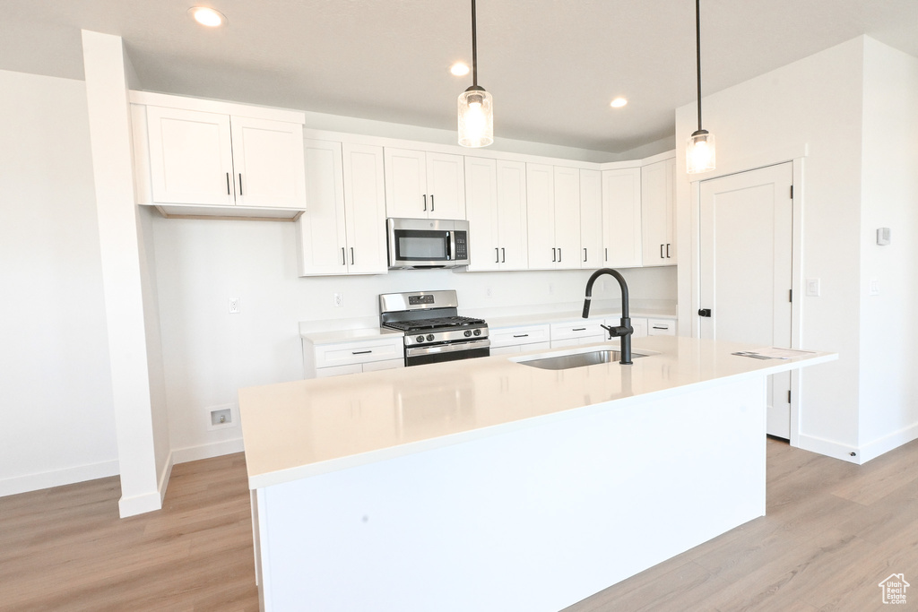 Kitchen featuring pendant lighting, light wood-type flooring, appliances with stainless steel finishes, sink, and an island with sink