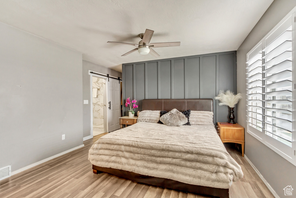 Bedroom featuring a barn door, light hardwood / wood-style floors, ceiling fan, and ensuite bathroom