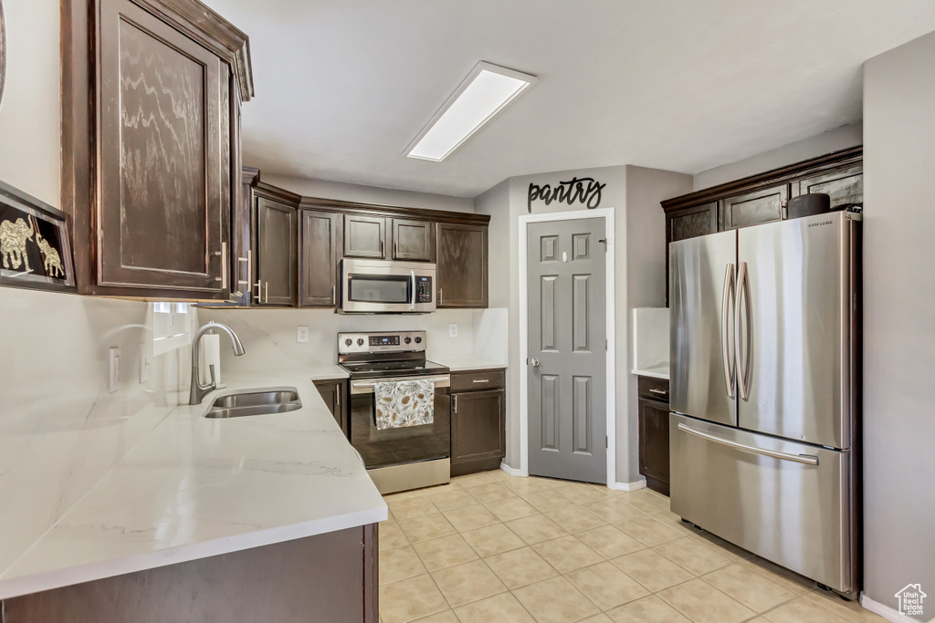 Kitchen with light tile flooring, appliances with stainless steel finishes, sink, and light stone counters