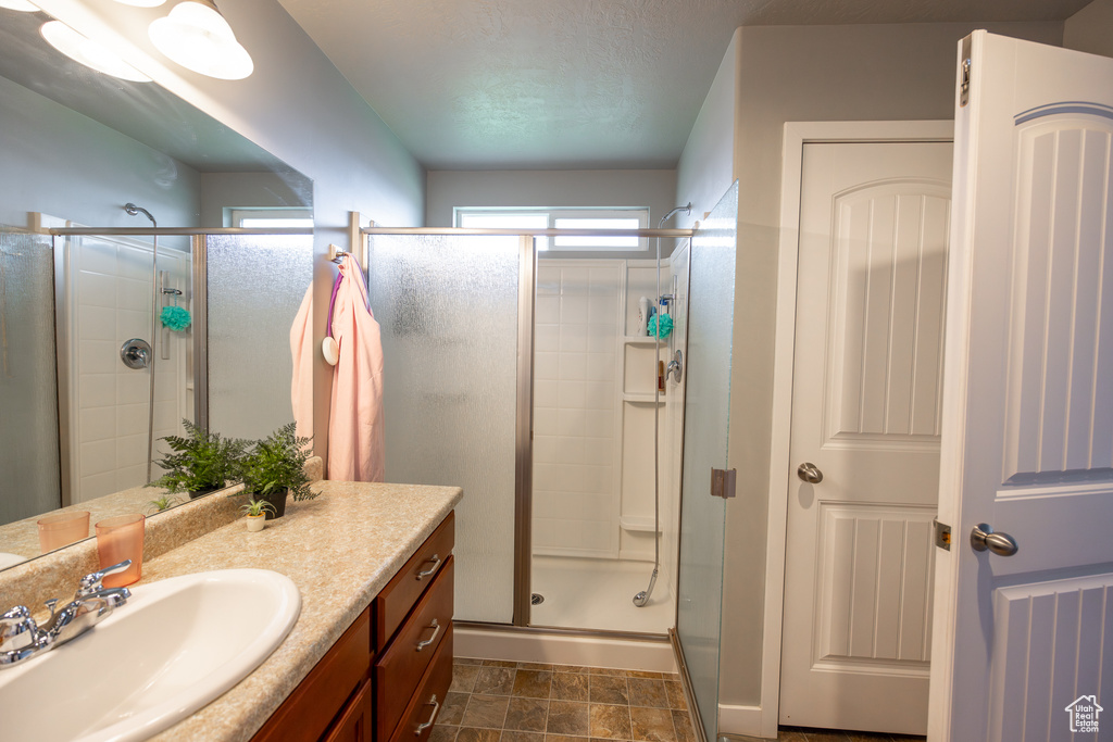 Bathroom with large vanity, a shower with shower door, and tile flooring