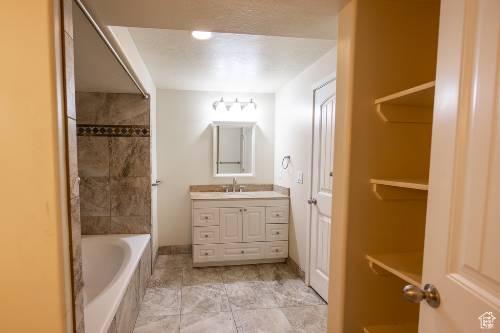 Bathroom featuring a bath to relax in, tile floors, vanity, and a textured ceiling