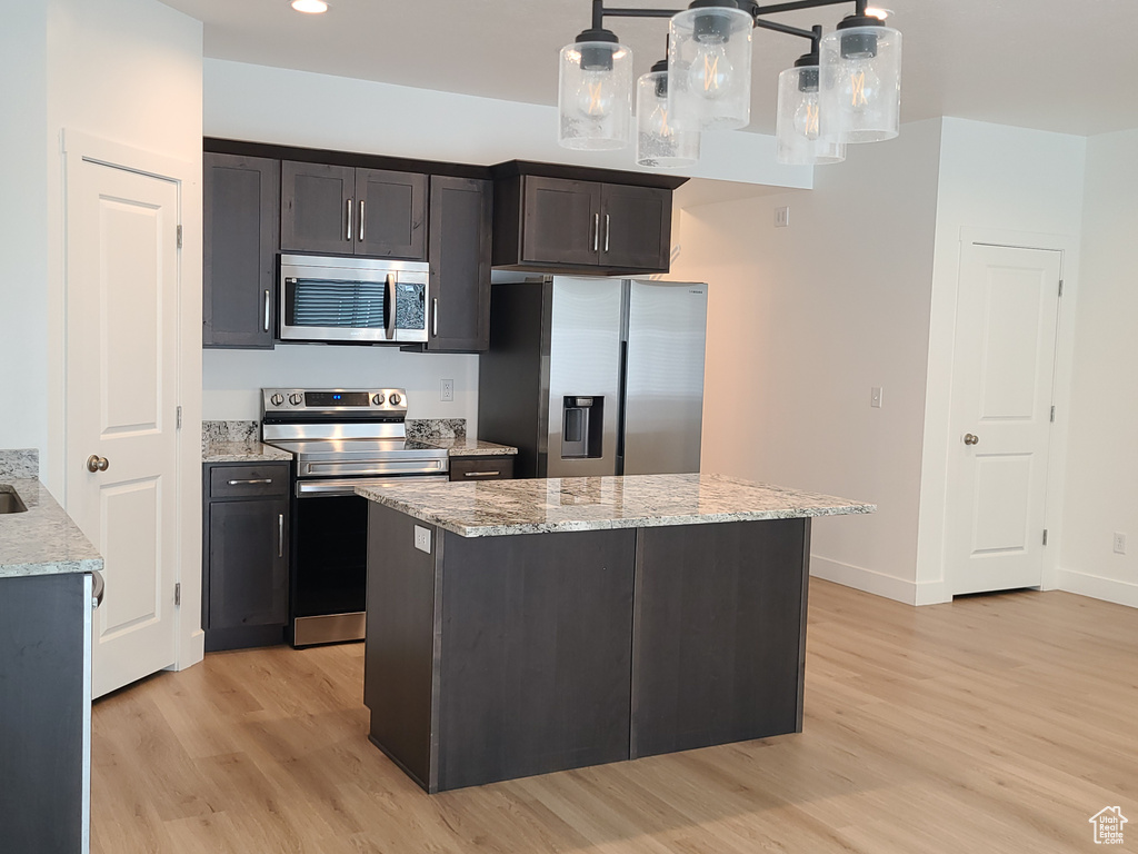 Kitchen with a center island, light hardwood / wood-style floors, hanging light fixtures, stainless steel appliances, and light stone countertops