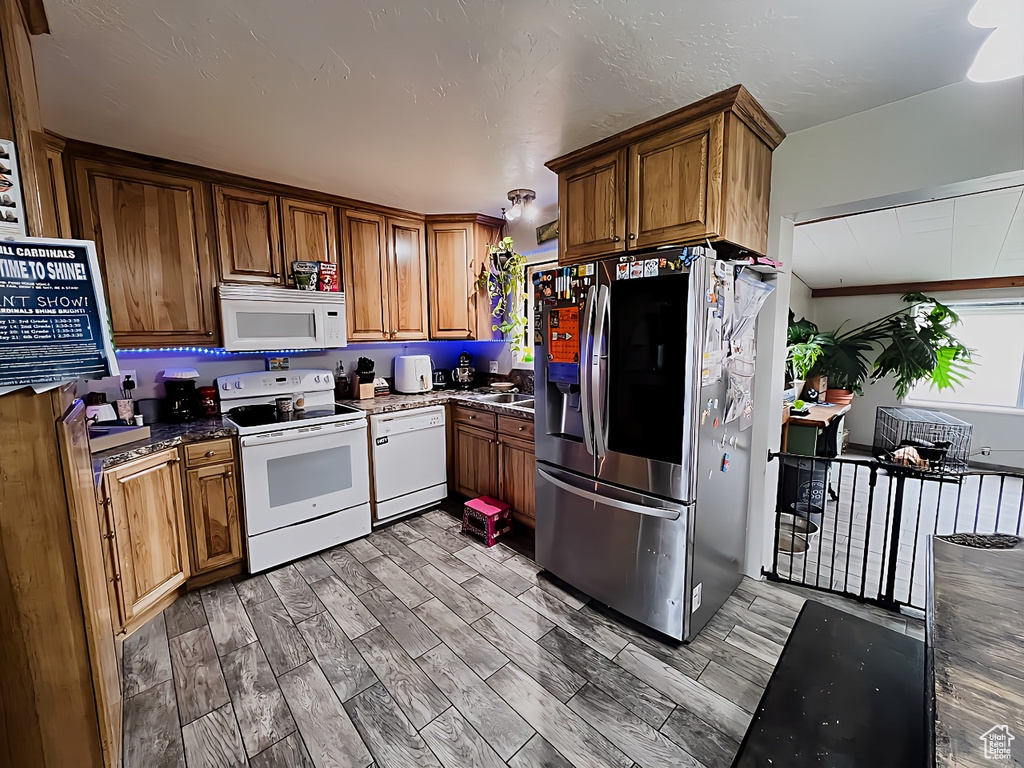 Kitchen featuring wood-type flooring, white appliances, sink, and dark stone countertops
