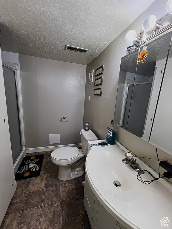 Bathroom featuring tile flooring, a textured ceiling, toilet, vanity, and a shower with door