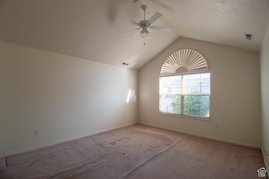 Empty room featuring lofted ceiling, ceiling fan, a textured ceiling, and carpet flooring