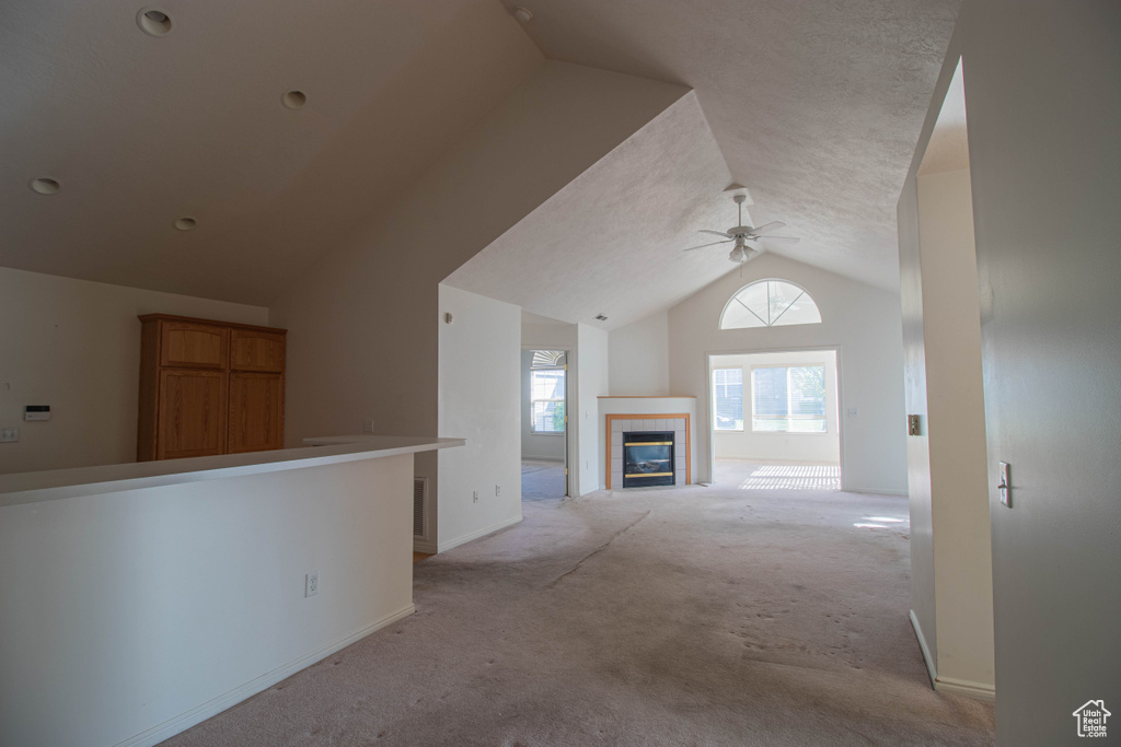 Additional living space with light colored carpet, ceiling fan, lofted ceiling, a textured ceiling, and a tile fireplace