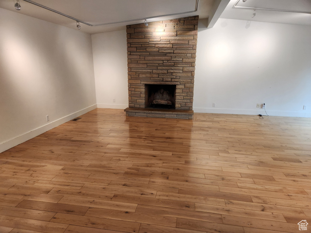 Unfurnished living room with wood-type flooring, track lighting, and a stone fireplace