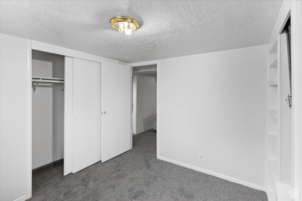 Unfurnished bedroom with a closet, a textured ceiling, and dark colored carpet
