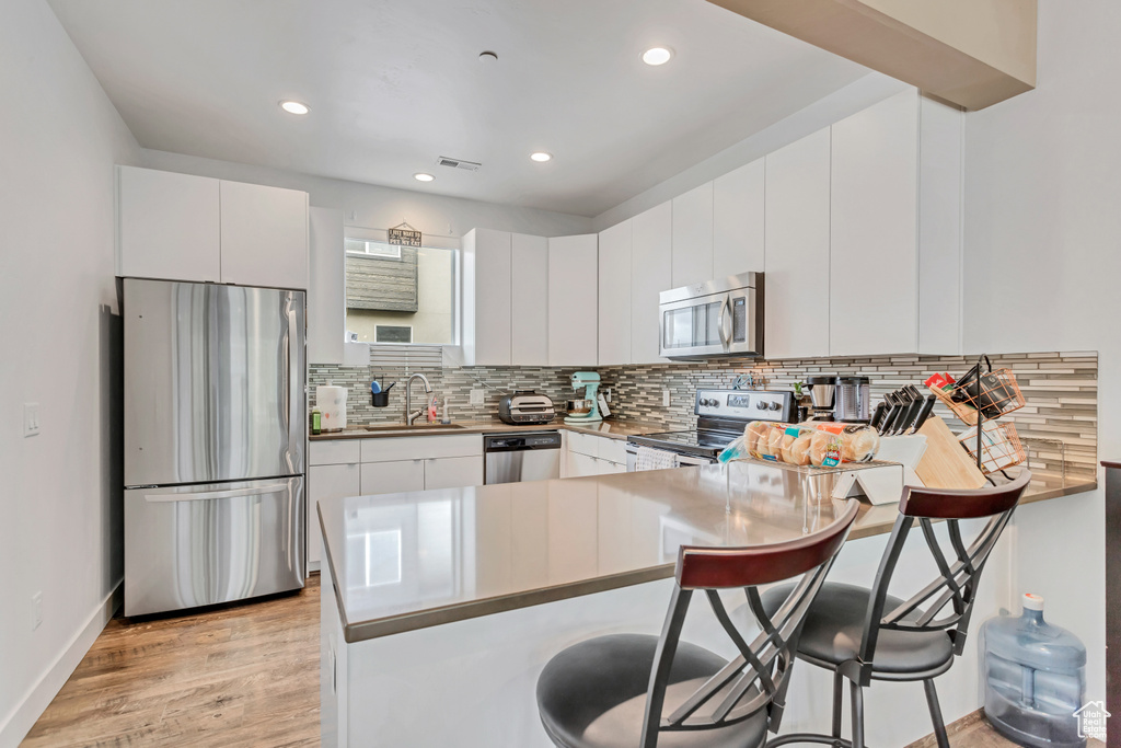 Kitchen with appliances with stainless steel finishes, white cabinets, tasteful backsplash, light hardwood / wood-style flooring, and a kitchen breakfast bar
