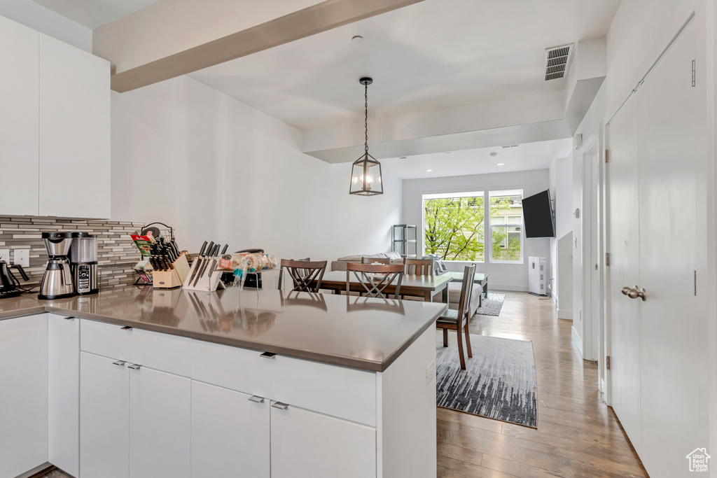 Kitchen featuring white cabinets, tasteful backsplash, light wood-type flooring, a chandelier, and pendant lighting