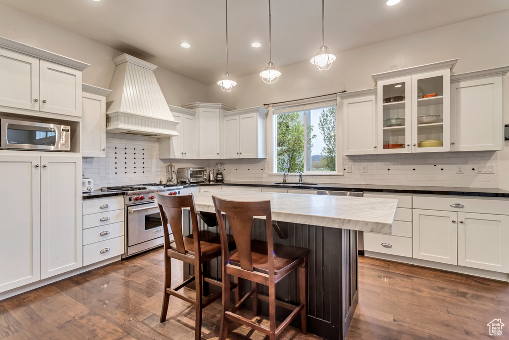 Kitchen featuring custom exhaust hood, dark hardwood / wood-style floors, backsplash, appliances with stainless steel finishes, and a kitchen island