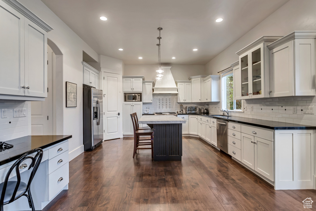 Kitchen with dark hardwood / wood-style flooring, custom range hood, stainless steel appliances, a kitchen island, and tasteful backsplash