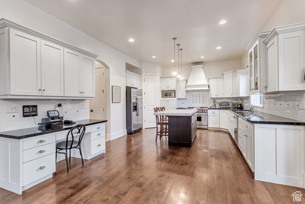 Kitchen featuring appliances with stainless steel finishes, a kitchen island, dark hardwood / wood-style flooring, premium range hood, and a kitchen breakfast bar