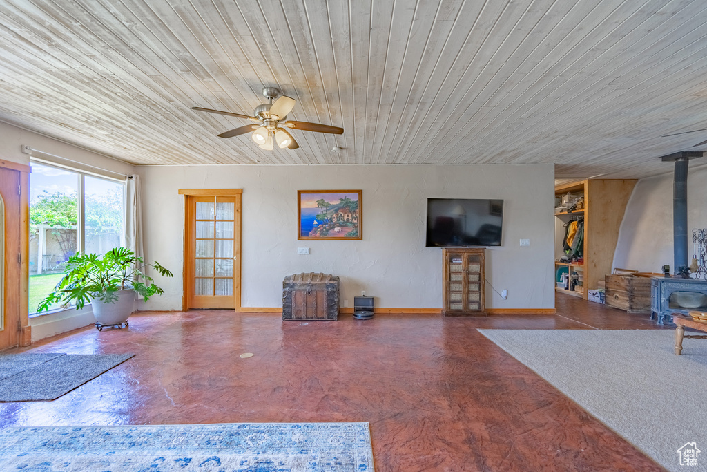 Unfurnished living room featuring a wood stove, ceiling fan, and wooden ceiling