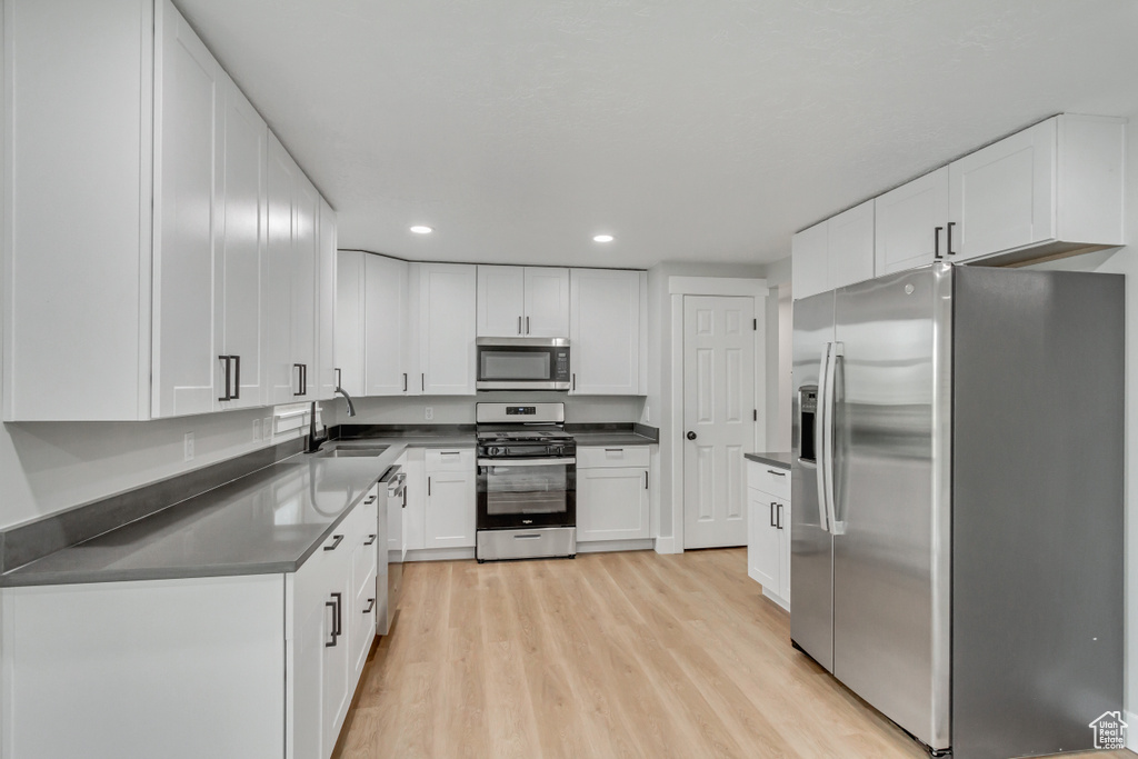 Kitchen featuring appliances with stainless steel finishes, light hardwood / wood-style flooring, white cabinets, and sink