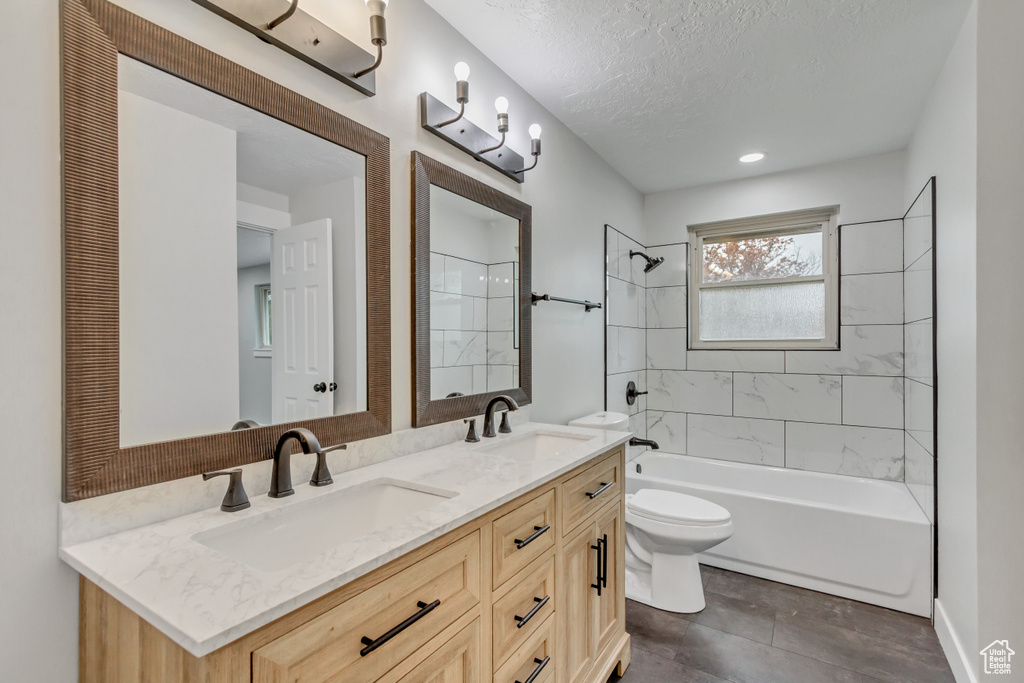Full bathroom with toilet, double vanity, tiled shower / bath combo, a textured ceiling, and tile floors