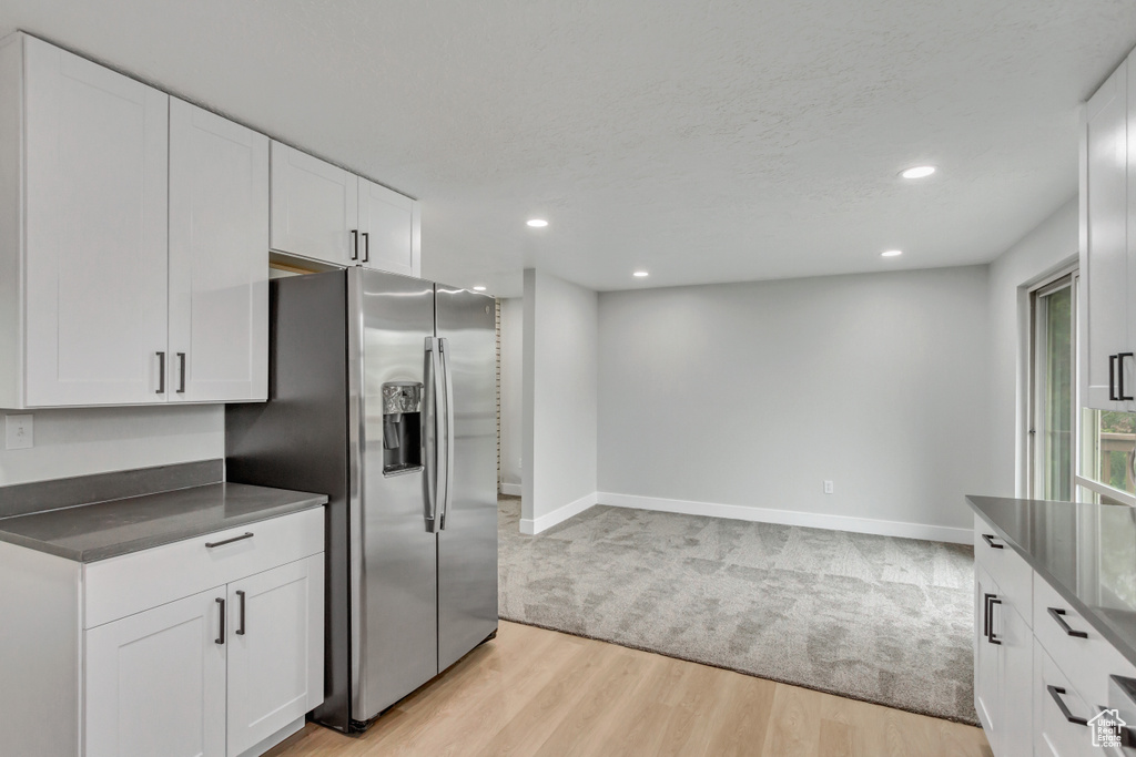 Kitchen featuring white cabinets, stainless steel refrigerator with ice dispenser, and light carpet