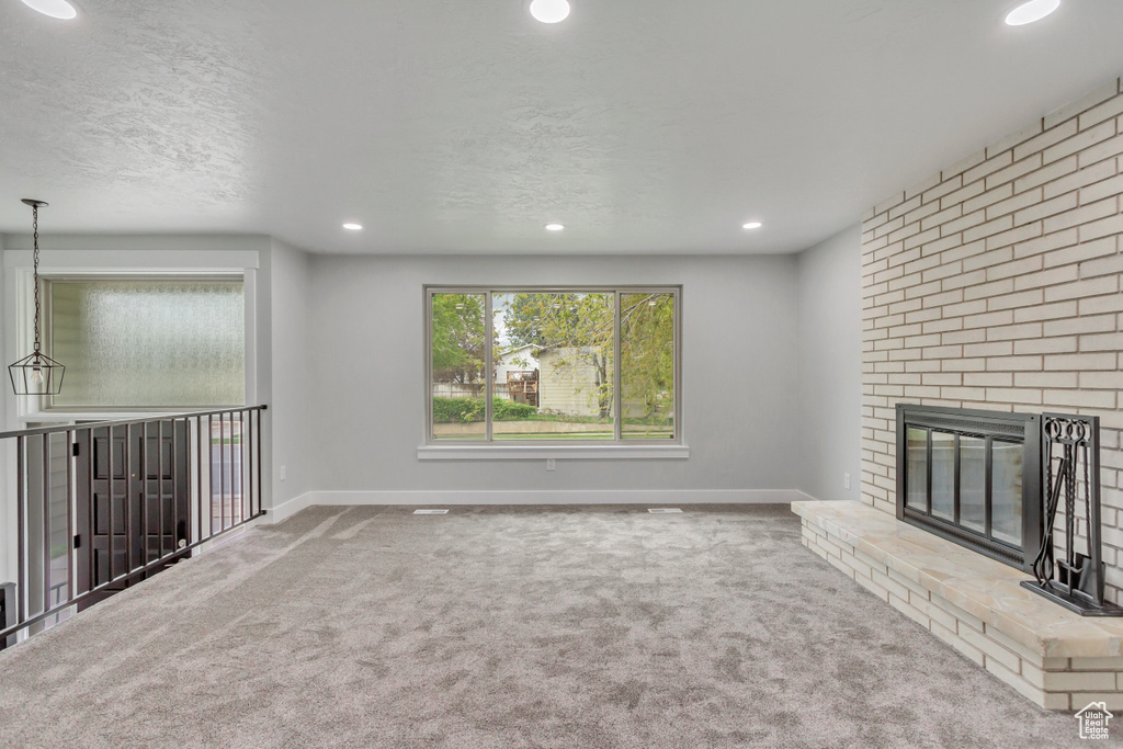Unfurnished living room with brick wall, a textured ceiling, carpet floors, and a fireplace