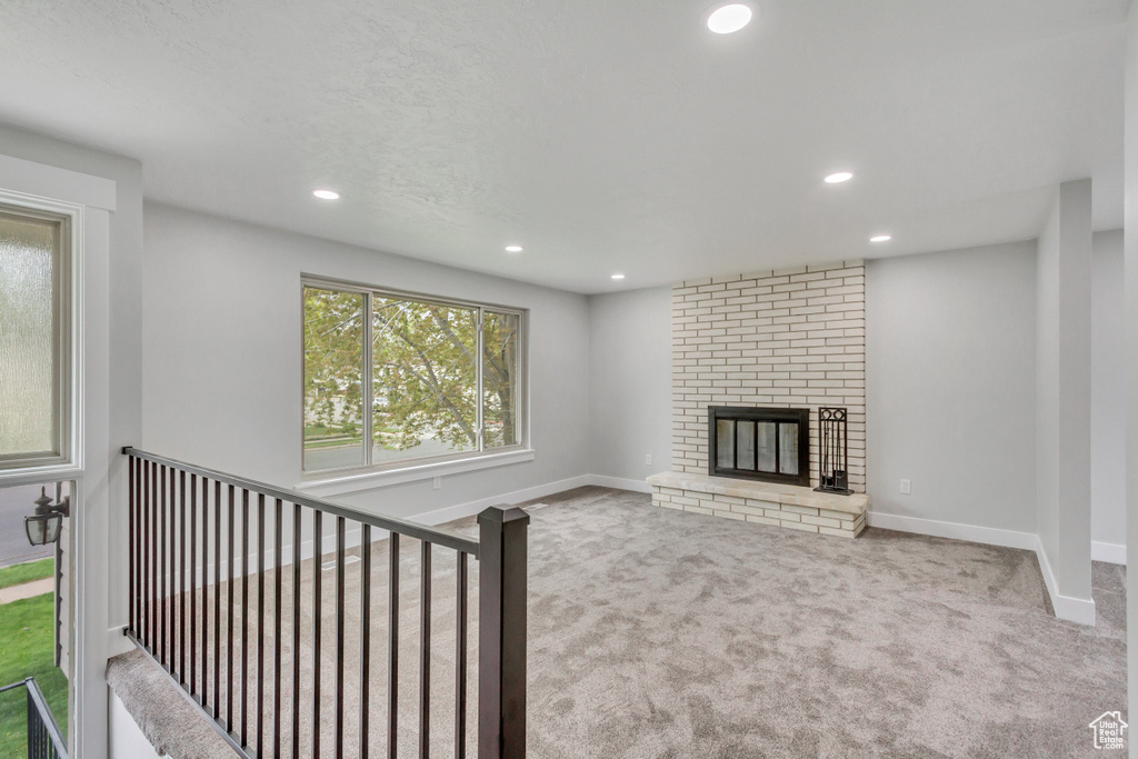 Unfurnished living room with a brick fireplace, brick wall, and carpet flooring