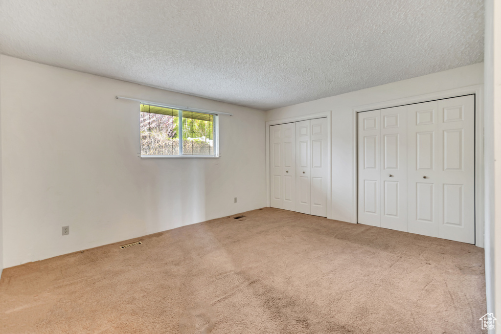 Unfurnished bedroom featuring two closets, carpet floors, and a textured ceiling