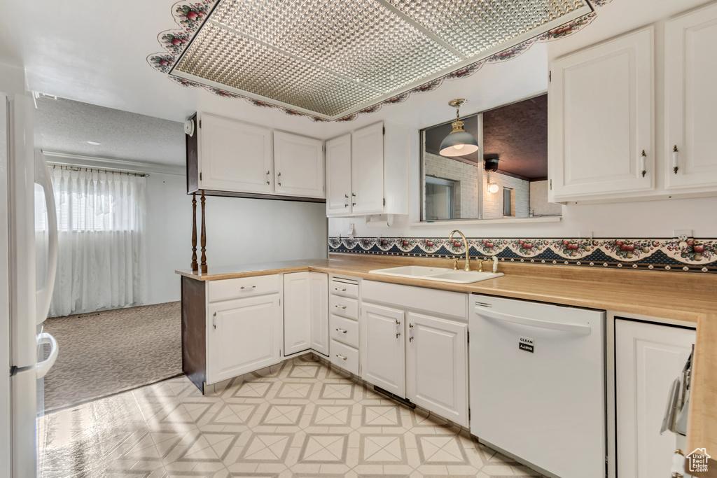 Kitchen featuring white appliances, white cabinetry, sink, pendant lighting, and light tile floors