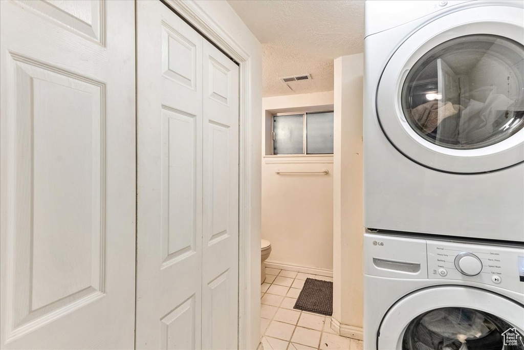 Clothes washing area featuring stacked washer and clothes dryer and light tile floors