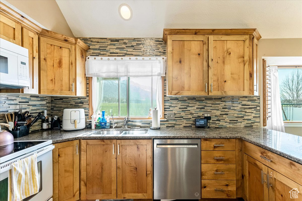 Kitchen with backsplash, dark stone counters, white appliances, and sink