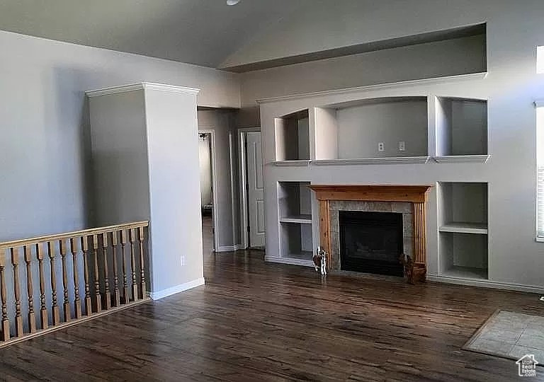Unfurnished living room featuring built in features, dark hardwood / wood-style floors, and a tiled fireplace