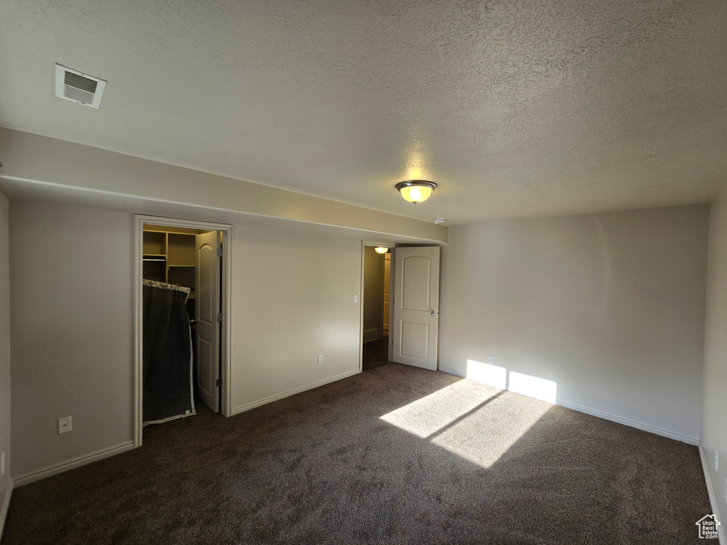 Unfurnished bedroom with a textured ceiling, a walk in closet, a closet, and dark colored carpet