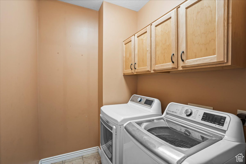 Laundry room with cabinets, light tile floors, and washer and clothes dryer