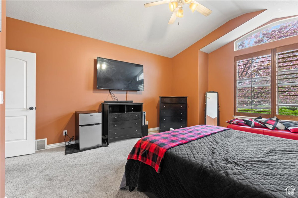Carpeted bedroom with lofted ceiling, ceiling fan, and stainless steel refrigerator