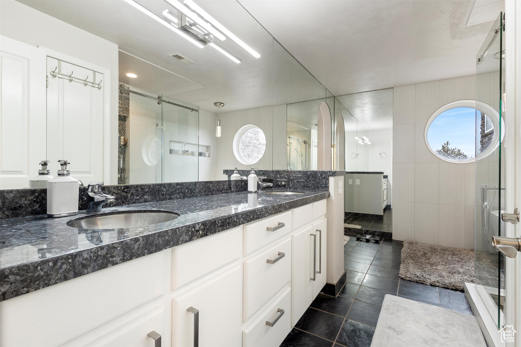Bathroom featuring a shower with door, oversized vanity, dual sinks, and tile flooring