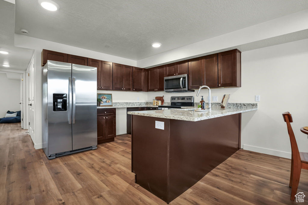 Kitchen with hardwood / wood-style floors, kitchen peninsula, stainless steel appliances, and light stone countertops
