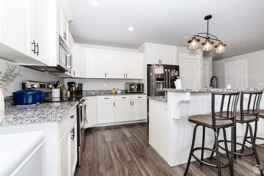 Kitchen featuring hanging light fixtures, stainless steel appliances, an island with sink, white cabinets, and dark hardwood / wood-style flooring