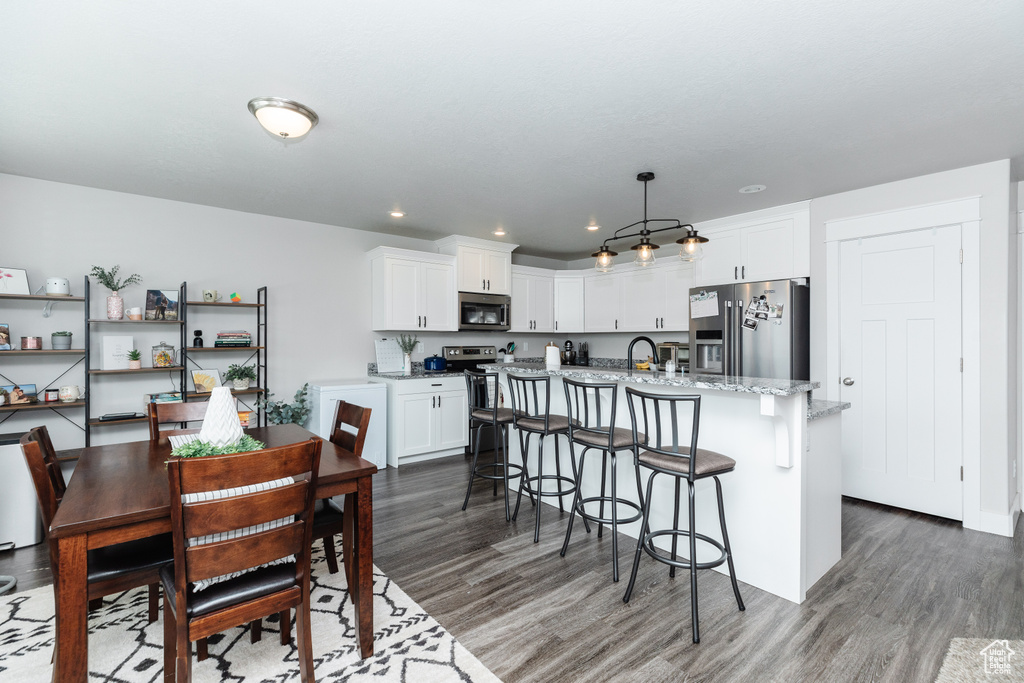 Kitchen featuring hanging light fixtures, stainless steel appliances, a center island with sink, white cabinetry, and hardwood / wood-style floors