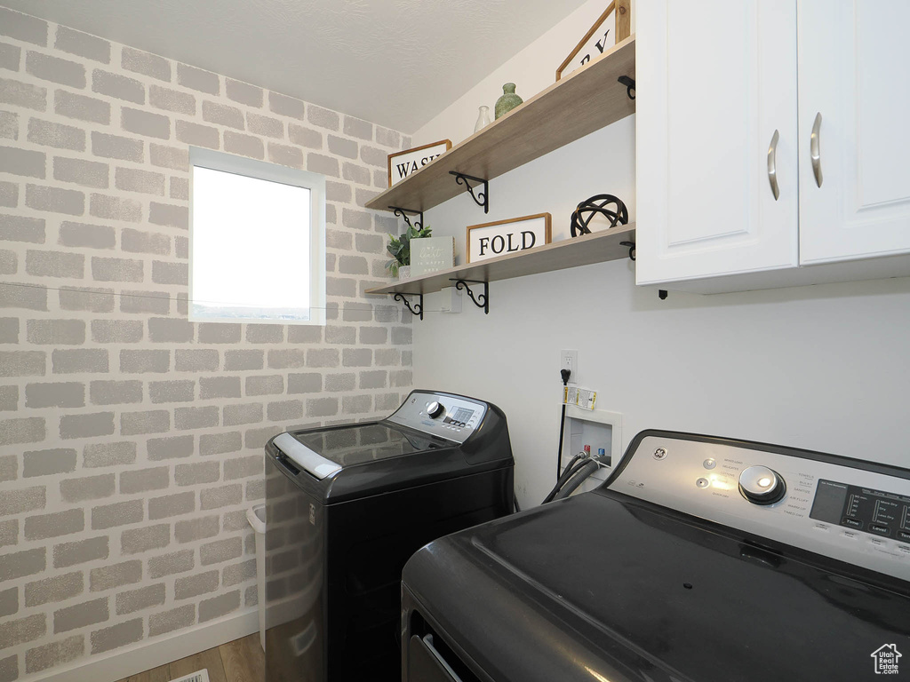 Clothes washing area featuring cabinets, hardwood / wood-style flooring, and washer / dryer