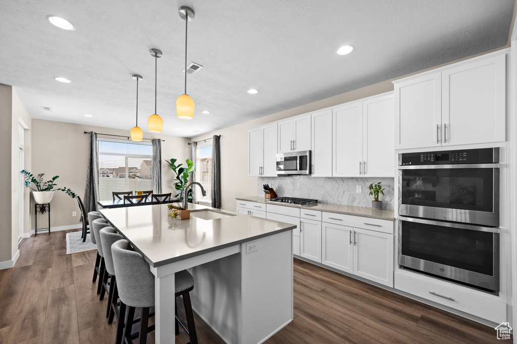 Kitchen featuring white cabinets, hanging light fixtures, appliances with stainless steel finishes, and dark wood-type flooring