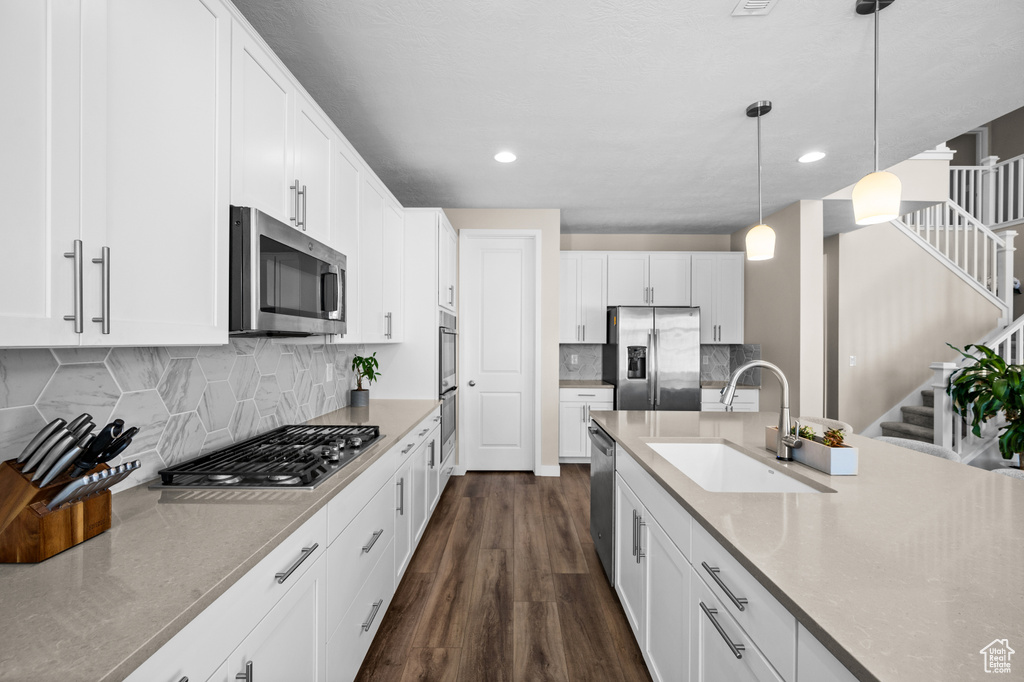 Kitchen featuring stainless steel appliances, dark hardwood / wood-style floors, white cabinetry, sink, and pendant lighting