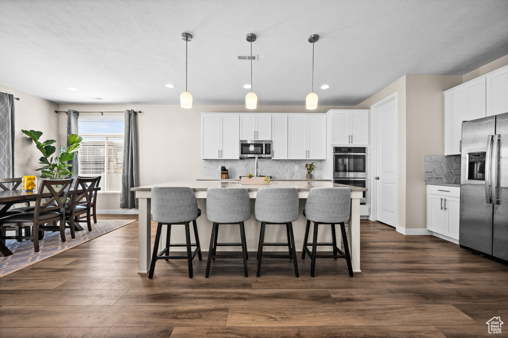 Kitchen featuring backsplash, appliances with stainless steel finishes, dark hardwood / wood-style flooring, and decorative light fixtures