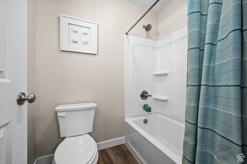 Bathroom featuring wood-type flooring, shower / tub combo with curtain, and toilet