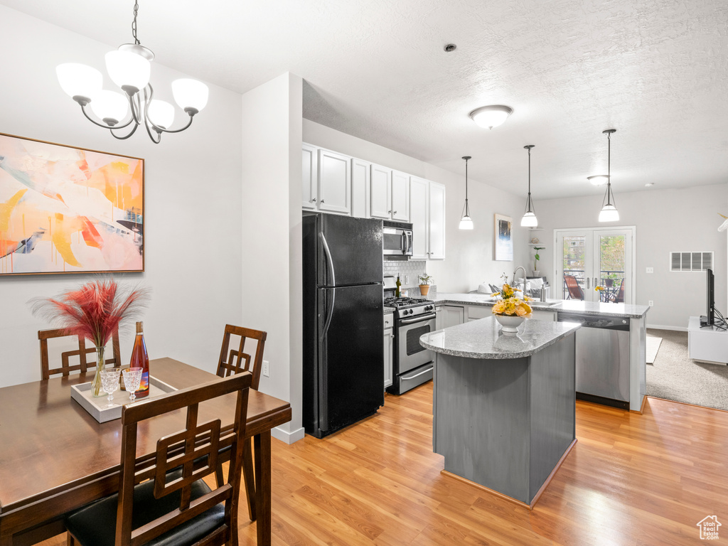 Kitchen featuring hanging light fixtures, light stone countertops, stainless steel appliances, and light hardwood / wood-style floors