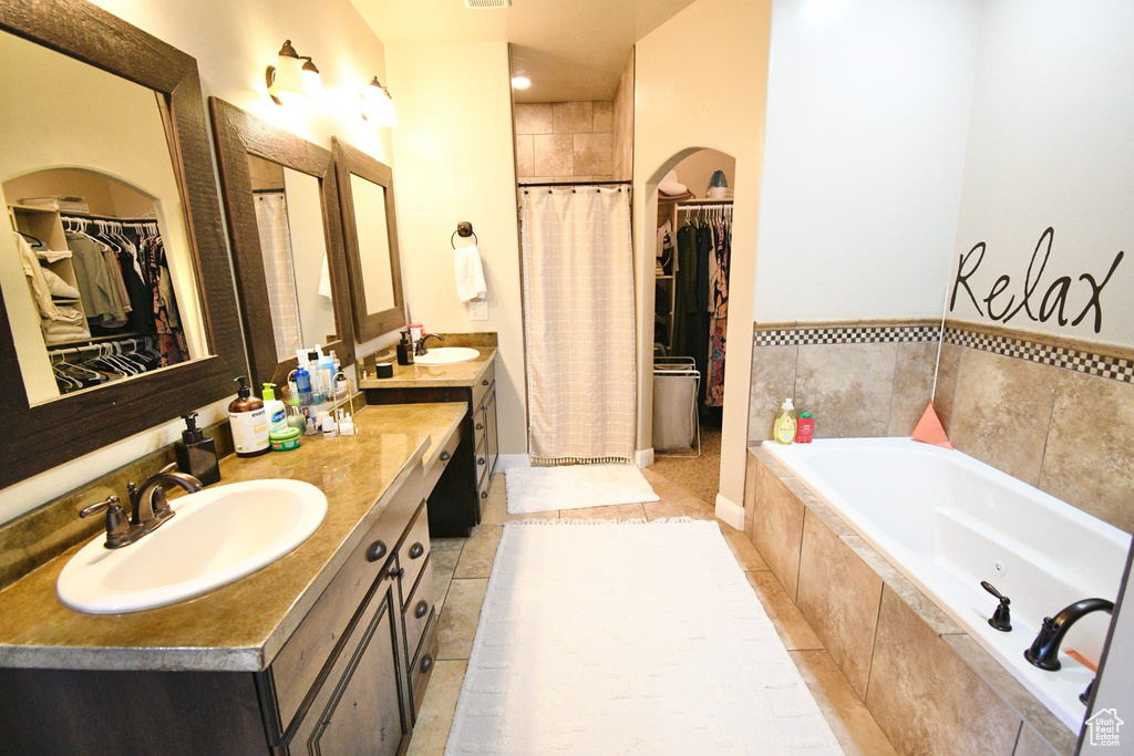 Bathroom featuring a relaxing tiled bath, vanity, and tile floors
